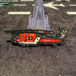 May include: A black, red, and white helicopter patch with the text "N411FA", "FIRE-RESCUE", and "ORANGE COUNTY FIRE AUTHORITY". The patch features a stylized helicopter design with a number 1 on the side and a small American flag.