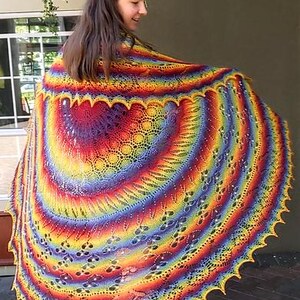 May include: A vibrant, rainbow-colored shawl with intricate lace patterns. The shawl features a scalloped edge and a circular design, showcasing a spectrum of colors from red to purple. This handmade accessory is perfect for adding a pop of color to any outfit.