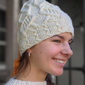 Pode incluir: Chapéu de malha creme com um design texturizado de malha de cabo. O chapéu é feito de um fio macio e quente e apresenta uma bainha canelada. Um acessório de inverno, perfeito para se manter aquecido no frio.