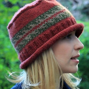 May include: A knitted cloche hat in shades of red, green, and gray. The hat features a ribbed brim and a patterned band around the crown. The hat is made of a soft, textured yarn, perfect for cooler weather.