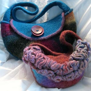 Könnte beinhalten: Eine handgefertigte Filzhandtasche mit blauem Korpus und Trageriemen, rotem Knopfverschluss und mehrfarbigem Streifendesign. Ein kleinerer, passender Filzbeutel mit Rüschenkante ist ebenfalls zu sehen.