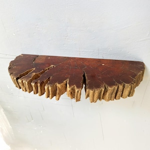 Puede incluir: Estante de madera rústico en forma de semicírculo con borde natural. El estante es de color marrón oscuro con vetas y grietas visibles. El borde tiene un aspecto rugoso y texturizado, resaltando la madera natural. Ideal para decoración.