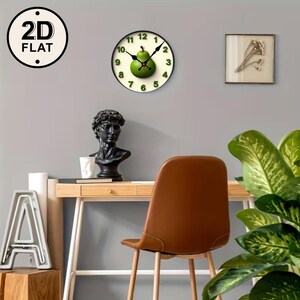May include: A round wall clock with a green pear design in the center. The clock has black hands and green numbers. The clock is mounted on a gray wall. The image also includes a desk, chair, and decorative items.