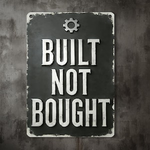 Könnte beinhalten: Ein rechteckiges, abgenutztes schwarzes Metallschild mit den Worten "BUILT NOT BOUGHT" in weißen Großbuchstaben. Oben befindet sich ein silbernes Zahnrad. Das Schild weist sichtbare Abnutzungserscheinungen auf.