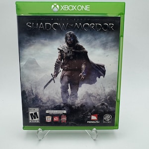 Puede incluir: Una caja de videojuego Xbox One de color verde para Middle-earth: Shadow of Mordor. La portada muestra a un personaje oscuro con armadura sosteniendo una espada en un paisaje desolado. La caja incluye la clasificación ESRB Mature 17+ y logotipos.