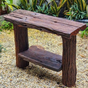 May include: A rustic, handcrafted wooden side table. The table features a dark brown, weathered tabletop and a lower shelf, supported by thick, textured wooden legs. The natural wood grain and knots are visible, giving it a unique, organic look. Perfect for a patio or garden.