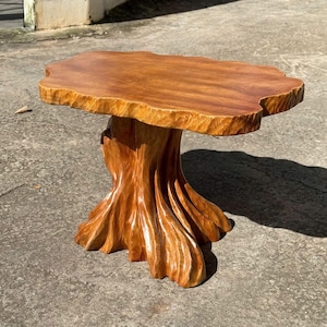May include: A handcrafted wooden side table with a unique tree trunk base and a natural edge top. The table is made of light brown wood and measures approximately 76 cm long, 51 cm wide, and 51 cm tall.