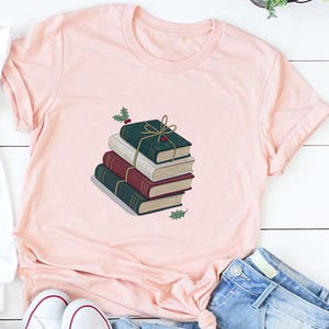 May include: White and heather peach t-shirts with a graphic of a stack of books tied with twine. The books are green, burgundy, and tan. The shirts are paired with blue jeans and white sneakers.