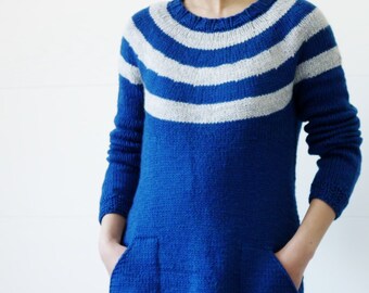 May include: A blue knitted dress with white stripes around the neckline. The dress has long sleeves and pockets.