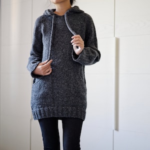 May include: A grey hooded sweater with a long, loose fit. The sweater is made from a soft, textured yarn and has a drawstring hood.