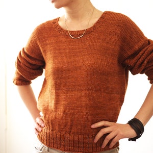 May include: A rust-colored knitted sweater with a round neckline. The sweater has a slightly loose fit and is made of a soft, textured yarn.