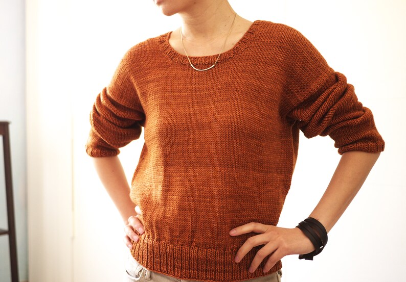 May include: A rust-colored knitted sweater with a round neckline. The sweater has a slightly loose fit and is made of a soft, textured yarn.