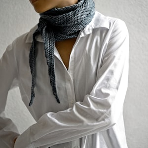 May include: A person wearing a white button-down shirt with a long, grey scarf tied around their neck.