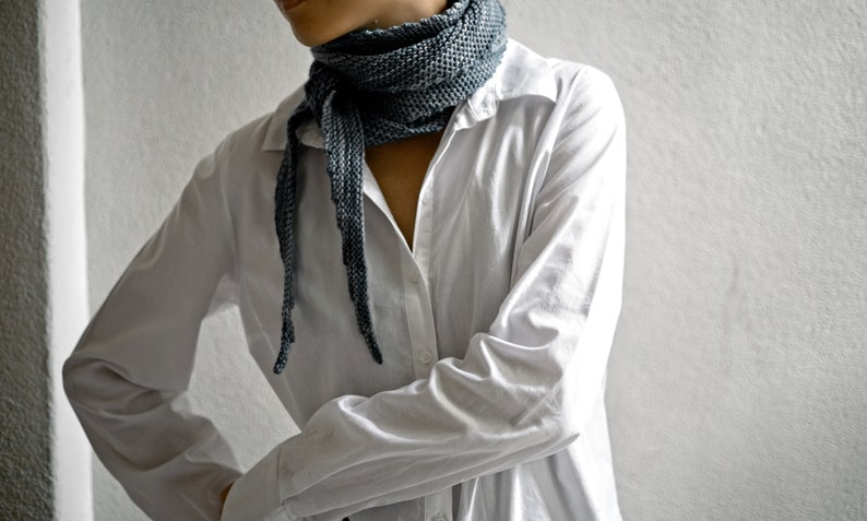 May include: A person wearing a white button-down shirt with a long, grey scarf tied around their neck.