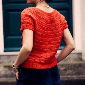 Può includere: Un maglione di lana rosso a maniche corte con un delicato motivo traforato. Il maglione ha una scollatura rotonda ed è realizzato con un filato morbido e leggero.