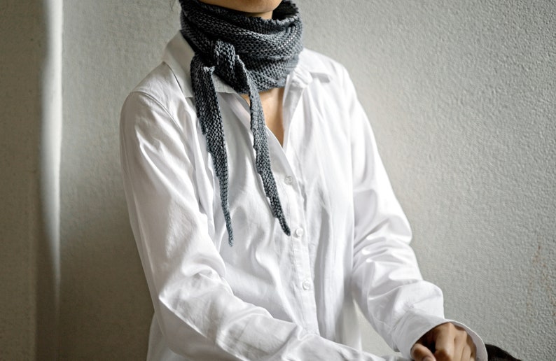 May include: A person wearing a white button-down shirt with a grey scarf tied around their neck.