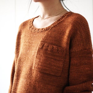 May include: A brown knitted sweater with a patch pocket on the front.