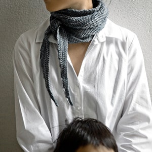 May include: A white button-down shirt with a long, grey scarf tied around the neck. The scarf has a textured, knitted pattern.