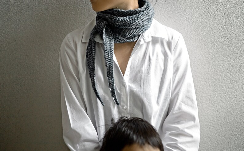 May include: A white button-down shirt with a long, grey scarf tied around the neck. The scarf has a textured, knitted pattern.