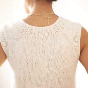 May include: White sleeveless knitted top with a round neckline. The top is made of a fine knit fabric and has a slightly loose fit.