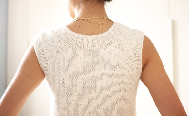 May include: White sleeveless knitted top with a round neckline. The top is made of a fine knit fabric and has a slightly loose fit.