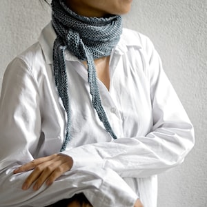 May include: A person wearing a white button-down shirt with a blue scarf tied around their neck.