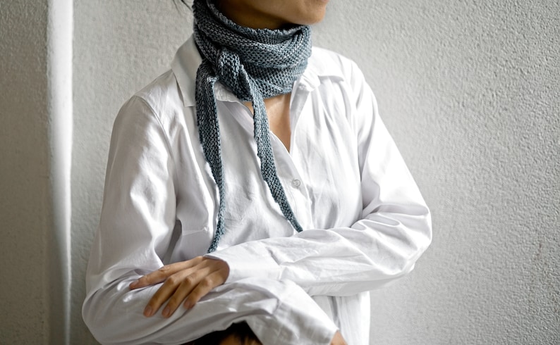 May include: A person wearing a white button-down shirt with a blue scarf tied around their neck.