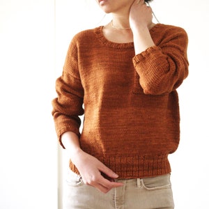 May include: A rust-colored knitted sweater with long sleeves and a crew neckline. The sweater is made of a soft, textured yarn and has a relaxed fit.