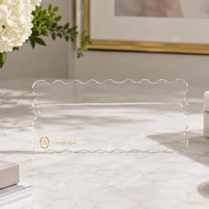 May include: A clear acrylic rectangular sign holder featuring a scalloped edge design. The center contains a horizontal slot for inserting paper. A small gold logo and the text "CAITLIN BYRN" are printed in the bottom left corner of the acrylic.
