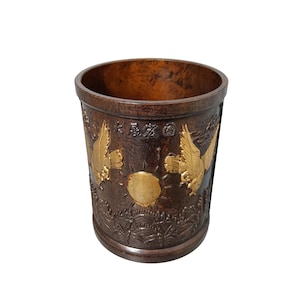 May include: A cylindrical, dark brown container with gold-colored eagle and sun designs. The container has a textured surface and a wide opening. The container has Chinese characters near the top.