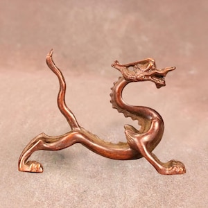 Peut inclure: Figurine de dragon de couleur bronze, dans une pose dynamique. Le dragon a un corps long et incurvé, des écailles détaillées et une expression féroce. La figurine mesure environ 15 cm de long.