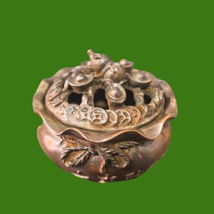 Peut inclure: Brûleur d'encens de couleur bronze avec un couvercle orné de motifs de pièces et d'lingots. Le brûleur a une base ronde et un motif floral détaillé. Le couvercle comporte plusieurs ouvertures et est surmonté d'une petite figurine animale.
