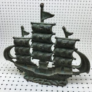 May include: A bronze-colored decorative ship sculpture with three masts and sails. The ship has a detailed design, including the hull, rigging, and flags. The sculpture is likely made of metal and has an aged appearance.