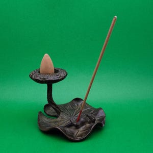 Puede incluir: Una taza de cerámica blanca con asa negra y el texto "But First, Coffee" en negrita negra. La taza se encuentra sobre un fondo borroso, sugiriendo un ambiente acogedor.