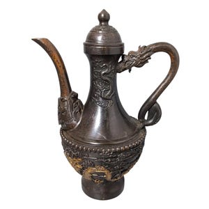 Peut inclure: Une cruche décorative de couleur bronze foncé avec des sculptures en relief complexes de dragons et de fleurs. La cruche présente un bec courbé, une poignée en forme de dragon et un couvercle avec un petit bouton. La base a des accents dorés.