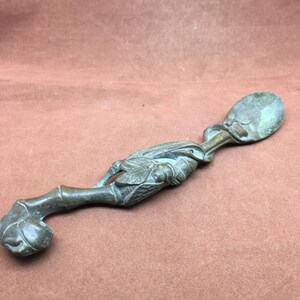 Op de afbeelding: Een bronzen lepel met een gedetailleerd insecten- en bamboe-ontwerp. De lepelkom is ovaal van vorm en de steel buigt met een bolvormig uiteinde. Het insect is ingewikkeld gesneden.