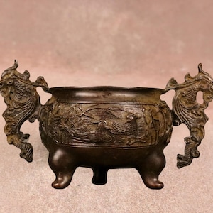 Op de afbeelding: Een witte keramische mok met een zwarte handgreep en de tekst "But First, Coffee" in een vetgedrukte, zwarte letter. De mok staat tegen een vage achtergrond, wat een gezellige setting suggereert.