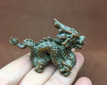 May include: A small, bronze-colored dragon figurine with intricate details. The mythical creature has a spiky spine, detailed scales, and a fierce expression. The dragon is posed in a dynamic stance, showcasing its legs and tail.