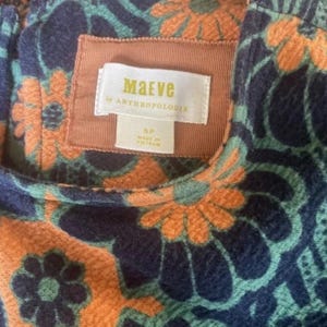 Op de afbeelding: Close-up van een stof met een patroon met een bloemmotief in oranje, teal en marineblauw. Het label luidt "Maeve by Anthropologie" en geeft maat 5P aan. Gemaakt in Vietnam.