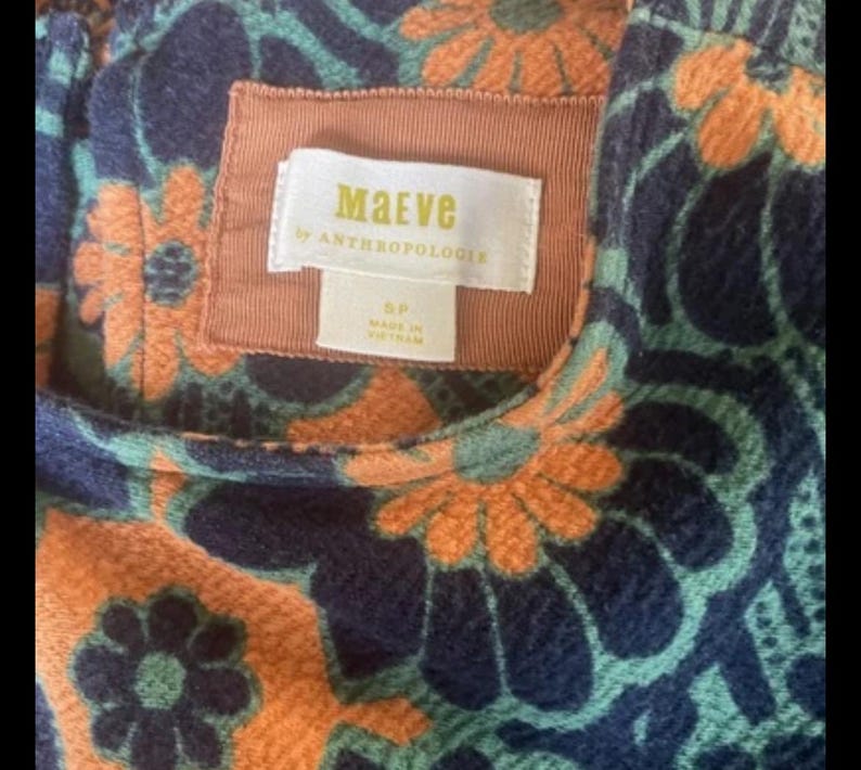 Op de afbeelding: Close-up van een stof met een patroon met een bloemmotief in oranje, teal en marineblauw. Het label luidt "Maeve by Anthropologie" en geeft maat 5P aan. Gemaakt in Vietnam.