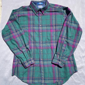 May include: A green, purple, and blue plaid button-down shirt. The long-sleeved shirt features a button-down collar and buttoned cuffs. The shirt is made of a soft, woven fabric. The shirt is laid flat on a light-coloured surface.