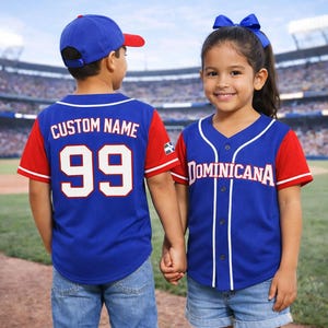 Puede incluir: Dos niños con camisetas de béisbol azules con mangas rojas. Las camisetas tienen ribetes blancos y la palabra "Dominicana" o "CUSTOM NAME". Una camiseta tiene el número 99. Ambos llevan gorras de béisbol.