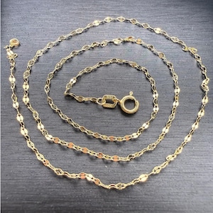 May include: A gold chain necklace featuring a series of interconnected, flattened oval links. The necklace includes a circular spring ring clasp and a small rectangular tag stamped with the text BSI and 10K, indicating the gold purity.