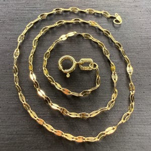 May include: A gold chain necklace featuring a series of elongated, oval-shaped links. The necklace includes a round spring ring clasp with a small rectangular tag attached, clearly stamped with the text BSI and 10K, indicating its gold purity.