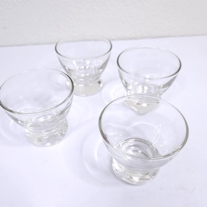 May include: Four clear, small, stemmed glasses with a rounded bowl shape. The glasses are made of transparent glass and sit on a white surface. The stems have a spiral design. The glasses are empty and appear to be clean.