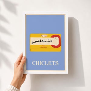 May include: A rectangular wall art print in a white frame featuring a light blue background with a yellow Chiclets gum box illustration in the center. The box displays Arabic text and the word CHICLETS in white capital letters at the bottom.