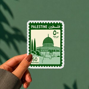 May include: A rectangular sticker featuring a postage stamp design with a dark green border. The center displays an illustration of the Dome of the Rock in dark green on a cream background. Text includes PALESTINE, Arabic script, and 50 POSTAGE.