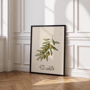 May include: A framed vertical wall art print featuring a botanical illustration of an olive branch with green leaves and olives on a textured beige background. Below the branch, black Arabic calligraphy text reads "والزيتون" with the number one.