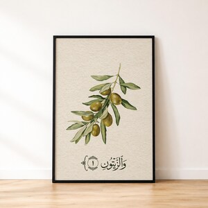 May include: A framed wall art print featuring a botanical illustration of an olive branch with green leaves and olives on a textured beige background. Below the branch, the Arabic text "والزيتون" is written alongside the number one in a circle.