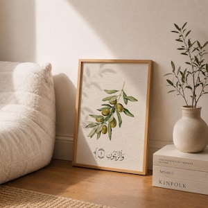 May include: A rectangular framed wall art print featuring a watercolor illustration of an olive branch with green olives and leaves. Below the branch, the Arabic text "والزيتون" is written in black calligraphy inside a decorative border.
